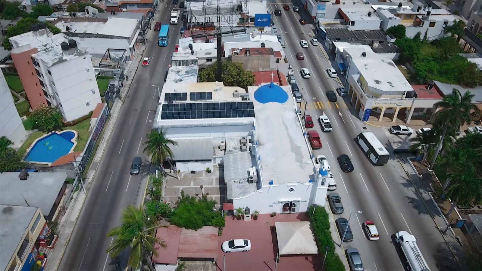 Vista aérea de un templo con cúpula azul junto a una avenida, con paneles solares instalados sobre la azotea contigua.